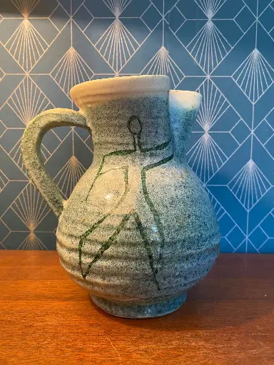 Accolay, superbe pichet des années 50, signé dans la masse, en excellent état. A noter une micro égrenure sur le col. Très belle pièce à décor d'un personnage au style naïf,  dans les tons de vert dégradé. Céramique émaillée et gondolée sur le tour et qui mesure 20cm de hauteur pour 18 au plus large.                                      Accolay, superb pitcher from the 1950s, signed in the mass, in excellent condition. Note a micro chip on the neck. Very beautiful piece decorated with a character in a naive style, in shades of shaded green. Glazed ceramic and warped on the rim, which measures 20cm in height and 18 at its widest.